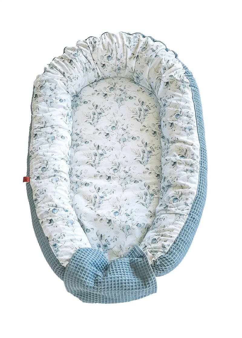 zweifarbiges Babynest: die eine Seite hat ein glattes Eukalypus-Muster und die andere einen grünen Waffelstoff